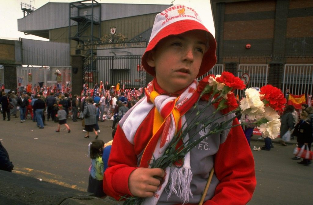 1989: A young unhappy Liverpool supporter carries some flowers in his team's colours to lay in tribute after the Hillsborough disaster at Anfield in Liverpool, England. Mandatory Credit: Pascal Rondeau/Allsport